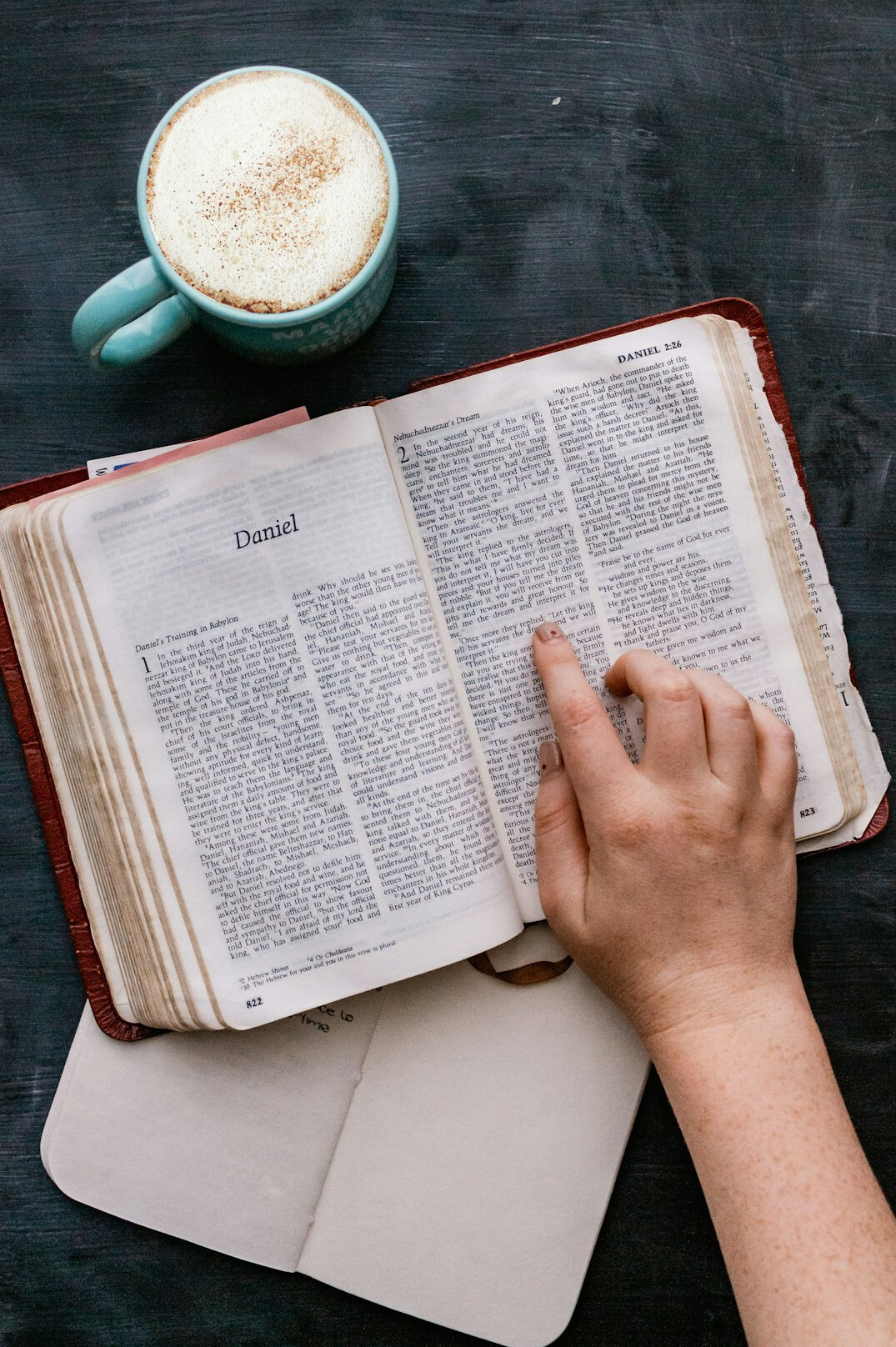 Hand writing notes in a notebook next to a cup of coffee